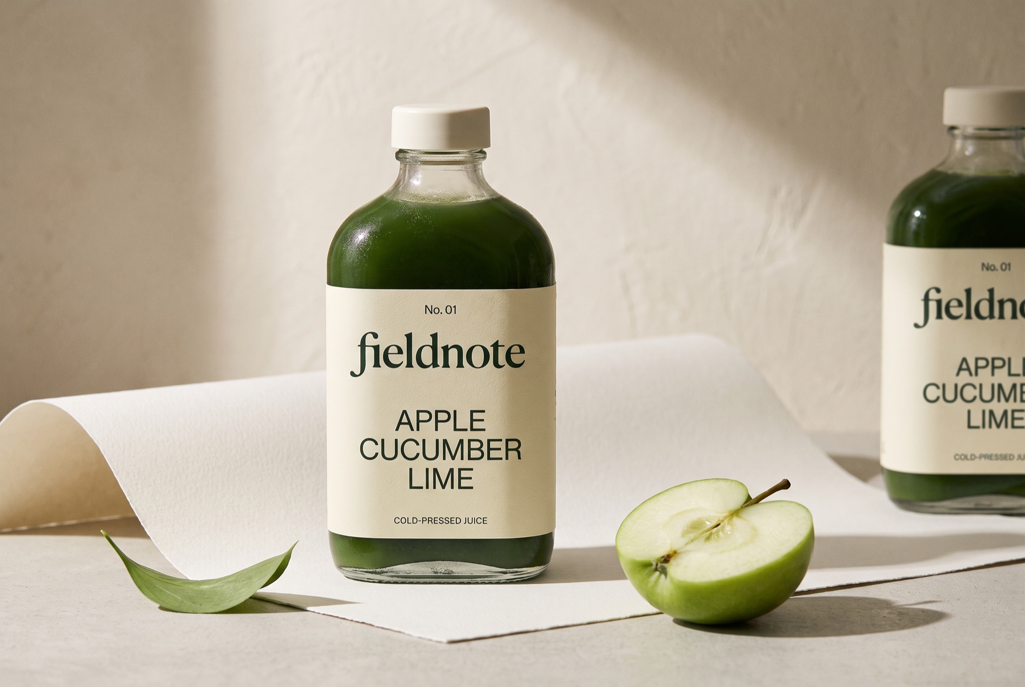 FIELDNOTE green juice in clear bottles with cream labels, a green apple and gently folded paper.