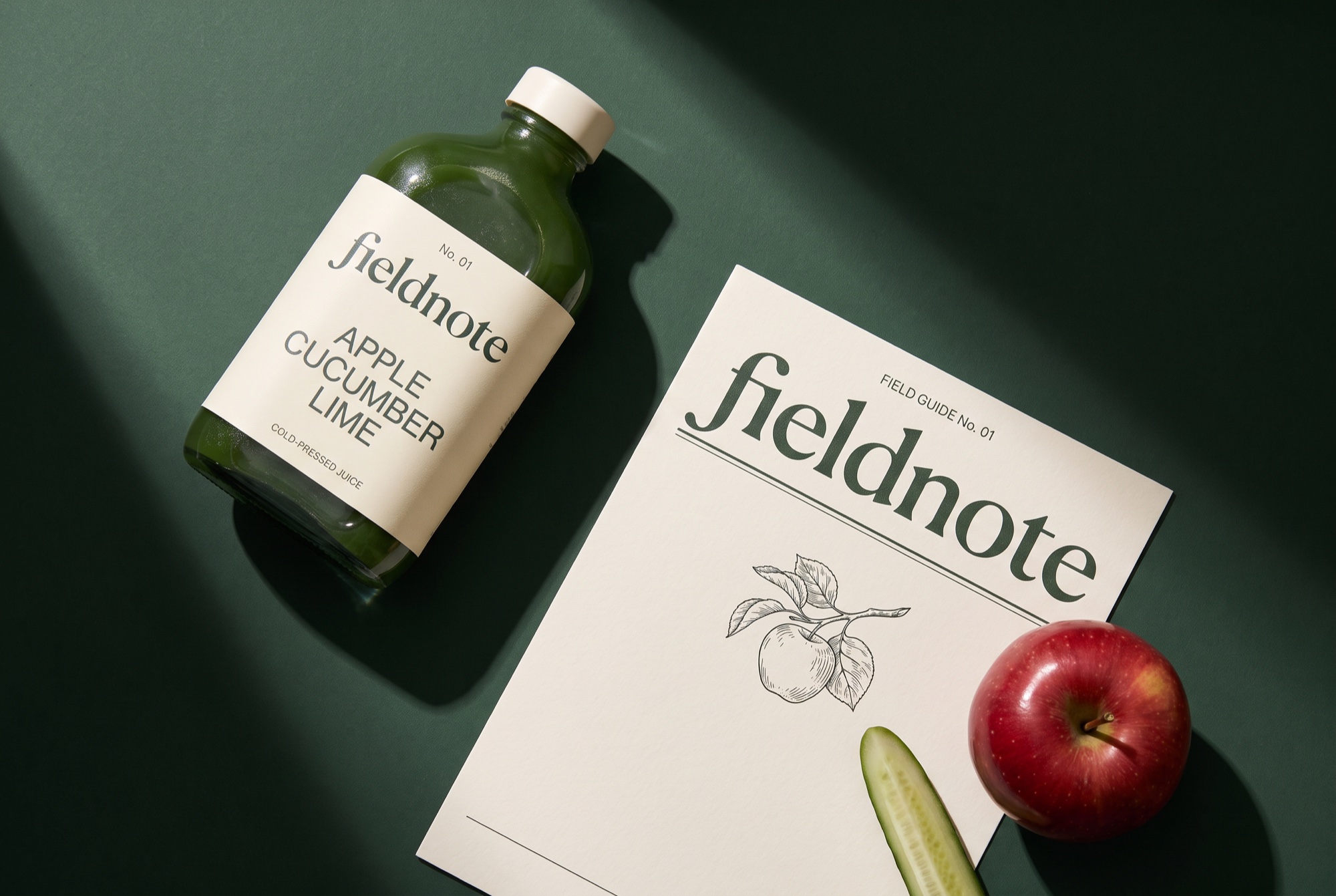 FIELDNOTE juice and a printed field guide arranged on a deep green tabletop.